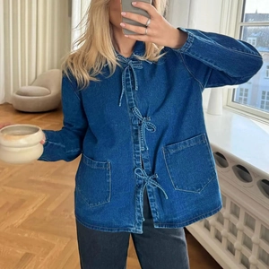 Détail de la veste en jean avec trois nœuds papillons et de grandes poches symétriques