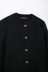 Gros plan sur la veste en tweed noir avec boutons dorés en forme de nœud et texture