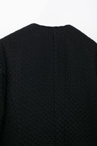 Gros plan sur le tissu en tweed noir texturé et la couture arrière de cette veste femme