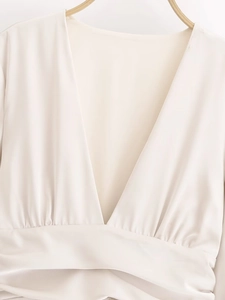 Detail eines eleganten cremefarbenen Satinkleids mit V-Ausschnitt und Taillenfalten