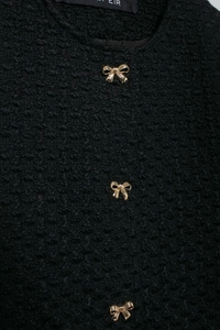 Détail d'une veste en tweed noir avec boutons en métal doré en forme de nœud et texture