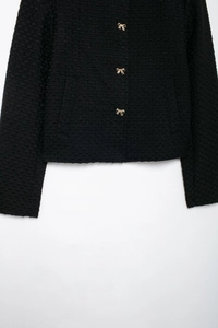 Détail d'une veste en tweed noir avec boutons dorés en forme de nœud et texture de tissu élégante
