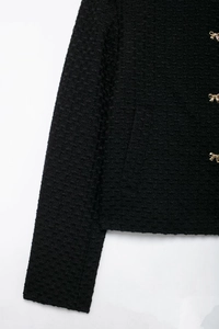 Vue détaillée de la texture du tweed noir et des boutons métalliques dorés en forme de nœud