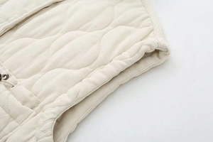 Detailed macro view of beige quilted vest fabric texture with wave-shaped stitching and seams