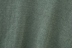 Macro detail of sage green knit fabric showing fine flat stitch texture and soft wool material