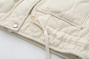 Detailed view of cream quilted vest showing drawstrings and silver metallic buttons