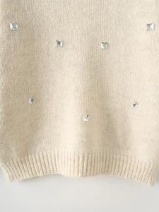 Close-up of cream knit sweater showing sparkling rhinestone detail and ribbed hem texture