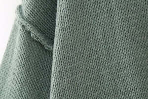Close-up of sage green chunky knit texture with detailed stitching on woman cardigan