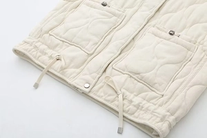 Detail of cream quilted vest featuring wavy stitching, metal snaps and adjustable drawstring