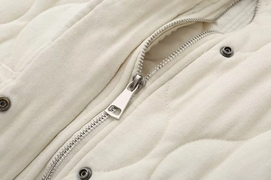 Close-up of quilted cream vest showing durable twill fabric and silver metal zipper detail
