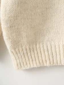 Close-up of ribbed knit cuffs on cream white sweater showing soft wool texture
