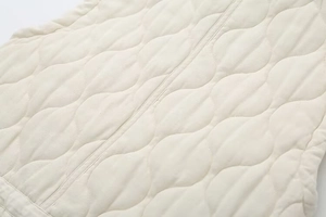 Detail of beige quilted vest featuring classic onion stitching and smooth metal zipper