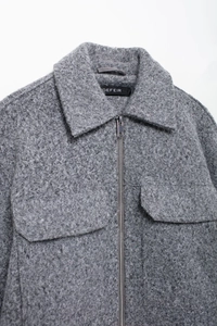 Close-up of grey textured wool blend jacket featuring silver zipper and flap chest pockets