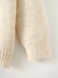 Close-up of cream knit sweater showing textured ribbed cuffs and soft fiber details