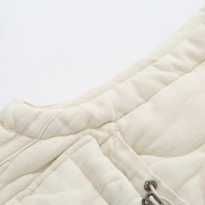 Close-up of cream quilted vest showing textured fabric, drawstring and metal hardware detail