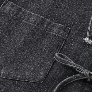 Détail de la texture denim noir délavé montrant la poche carrée et les coutures de chemise