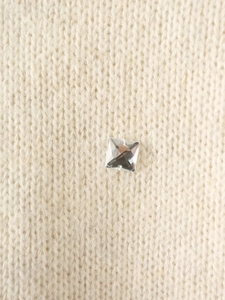 Close-up of a square faceted crystal rhinestone on an off-white knitted sweater fabric