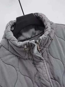 Detail view of gray quilted vest with stand-up collar, drawstring, and silver metal zipper