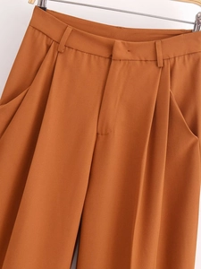 Detail of high-waist straight trousers featuring pleats and hidden zipper in caramel