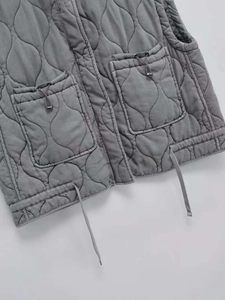 Detail of gray quilted vest featuring onion pattern stitching and large drawstring pockets