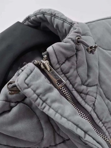 Detail of grey quilted vest featuring a stand-up collar with metallic zipper and drawstring