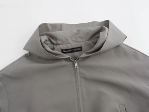 Dettaglio della giacca grigia con cappuccio, etichetta del marchio e trama del tessuto