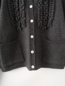 Close-up of dark grey knitted cardigan featuring ruffle trim details and white buttons