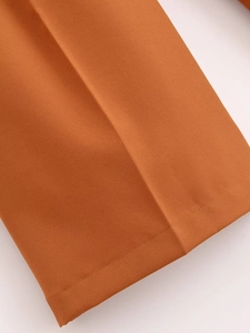 Close-up of orange straight-leg trousers showing pleated crease and hem stitching detail