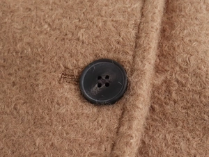 Macro shot of black four-hole button and textured camel sherpa wool fabric detail