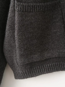 Detail of dark grey knit cardigan showing side pocket stitching and ribbed hem texture