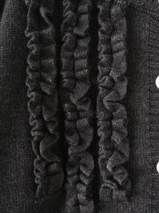 Detailed close-up of black knit fabric featuring elegant wavy ruffle layers and buttons