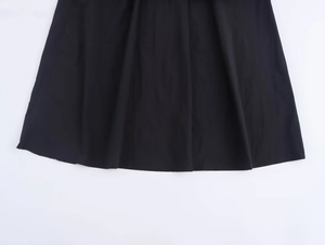Detail view of the pleated black skirt hem made from premium matte flat weave fabric