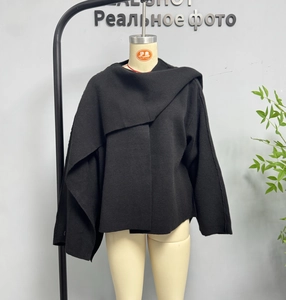 Detail of black knit shawl coat featuring asymmetric cut and thick texture on mannequin