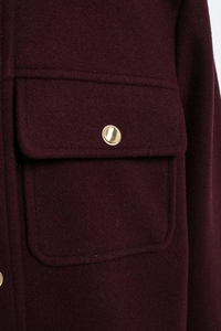 Detail of burgundy wool coat showing a pocket with a decorative gold metal button