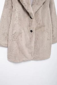 Detail of light grey faux fur coat featuring wide lapels and black button closure