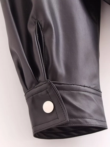Detailaufnahme der schwarzen Kunstlederjacke mit silbernem Metallknopf und feiner Naht