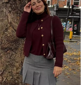 Detail view of burgundy knit cardigan with gold buttons and grey pleated skirt in London street
