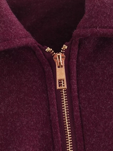 Detailed close-up of a burgundy wool jacket featuring a rose gold metallic zipper
