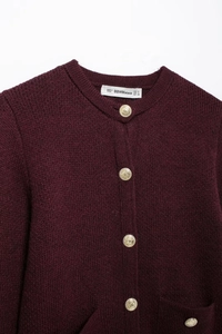 Detailed macro view of gold embossed buttons and woven texture on a burgundy cardigan