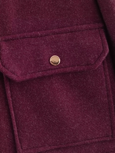 Detail of burgundy wool coat showing a textured pocket with a decorative gold button