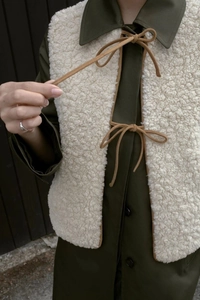 Detailed macro view of beige sherpa fleece vest with brown tie closures and soft texture