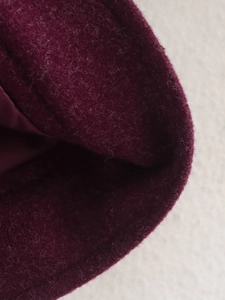 Detail of burgundy tweed fabric texture showing soft wool fibers and smooth inner lining