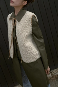 Detail of white sherpa fleece vest with brown drawstring tie over olive green coat