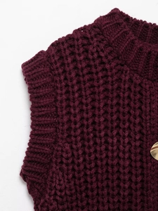 Detail of burgundy chunky knit vest featuring ribbed neckline and golden metal button