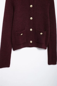 Detail of burgundy knit cardigan featuring textured fabric and embossed gold metal buttons