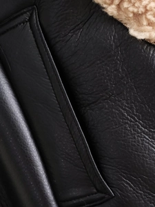 Gros plan d'un gilet en cuir noir avec doublure en peau de mouton beige et coutures