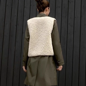 Back view of women's olive green long coat with cream fleece vest layered outfit