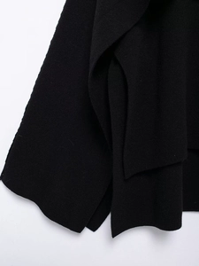 Detailed close-up of thick black knit fabric featuring a stylish side slit and hem finish