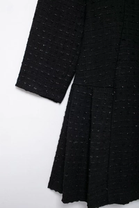 Détail du tissu en tweed avec fil argenté et jupe plissée sur une robe noire