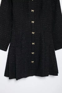 Détail d'une robe en tweed noir avec des boutons dorés en forme de nœud et plis